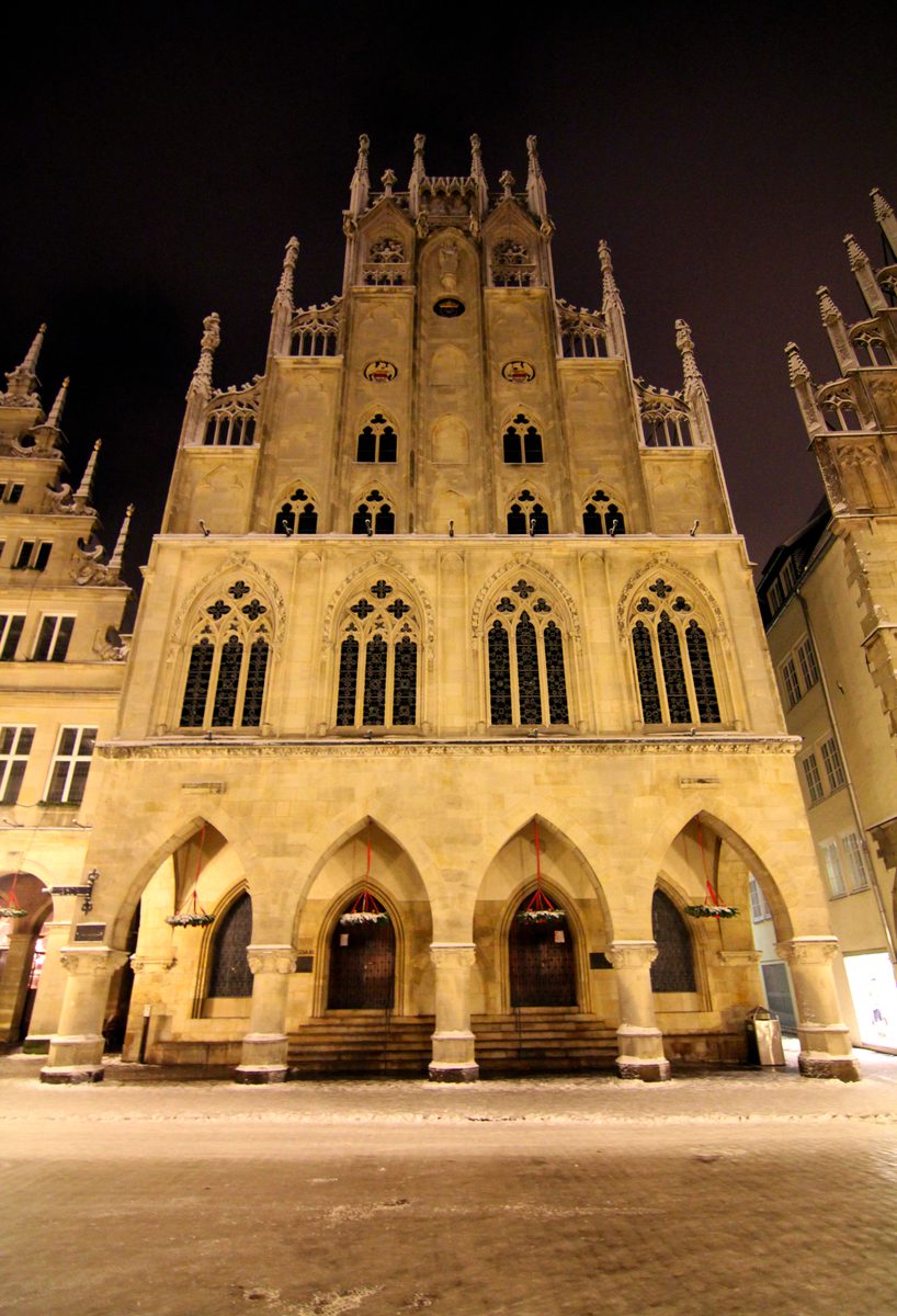 Die gotische Giebelfassade des Historischen Rathauses, golden beleuchtet bei Nacht, Schnee auf dem Pflaster