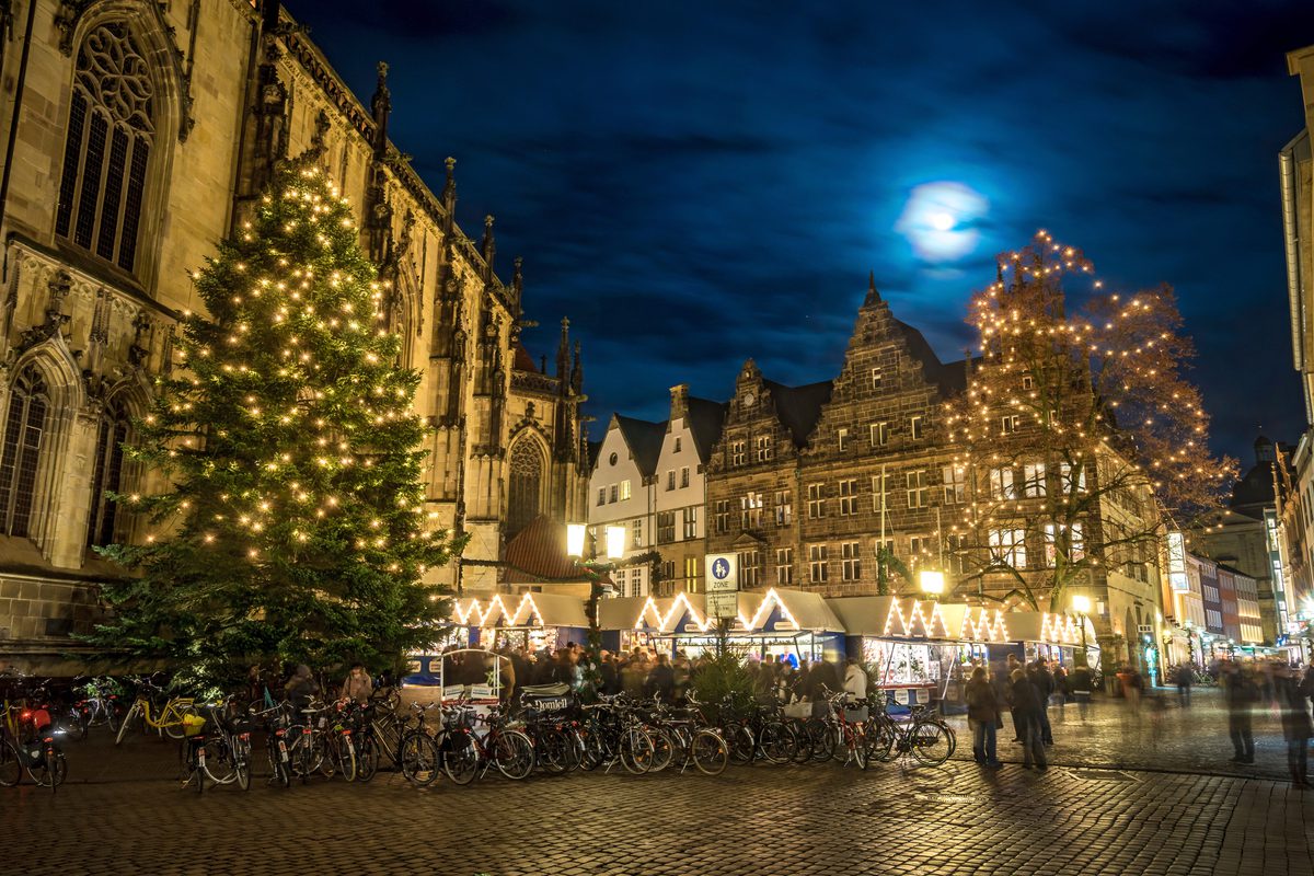 Weihnachtsmarkt am Prinzipalmarkt bei Nacht: beleuchteter Tannenbaum, Marktbuden, Giebelhäuser und der Vollmond