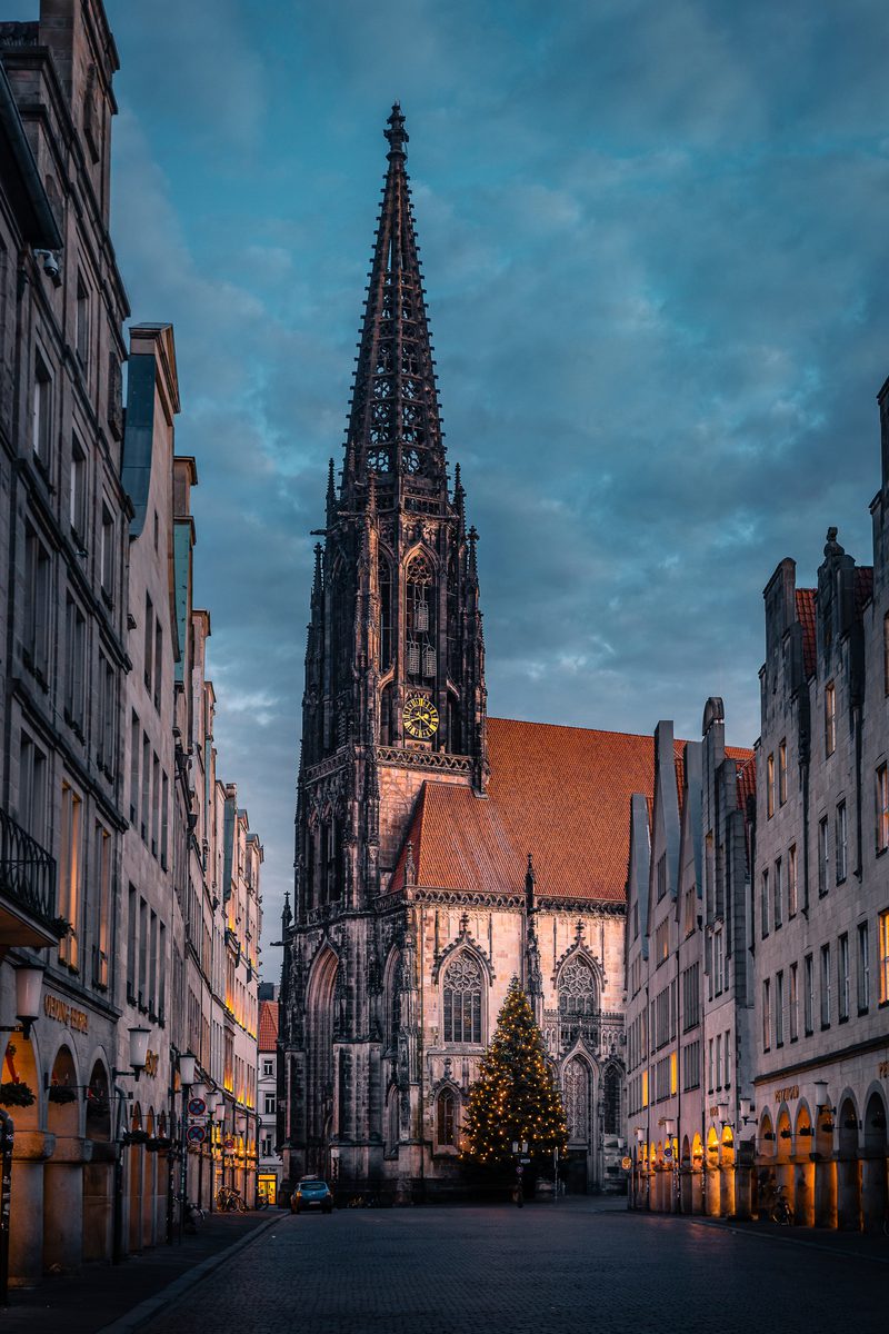 St. Lamberti am Ende der Giebelhäuser, davor der beleuchtete Weihnachtsbaum, Wolkenhimmel am Abend