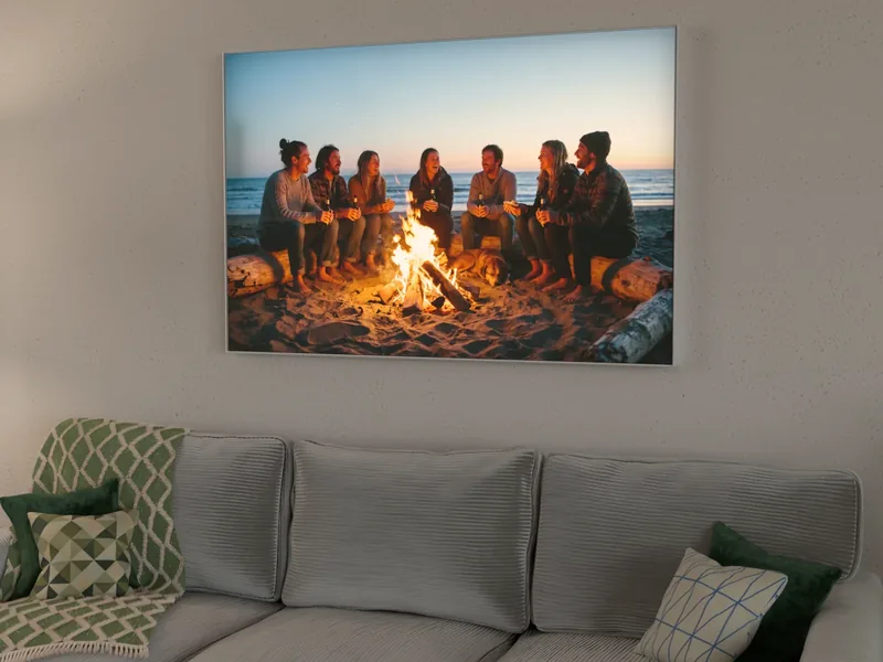 Visualisierung: eingeschaltetes Leuchtbild mit einem Lagerfeuerfoto am Strand über einem Sofa am Abend