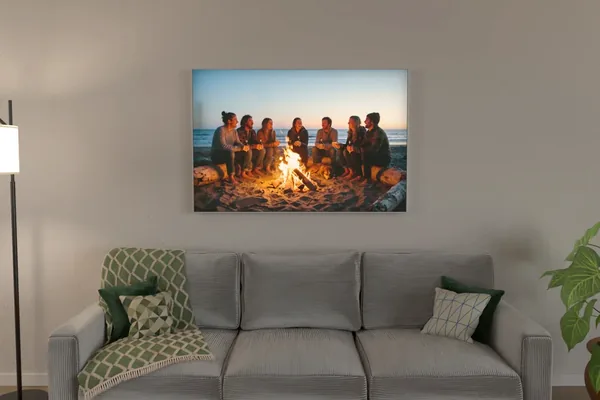 Visualisierung: Lagerfeuerfoto am Strand als eingeschaltetes Leuchtbild über einem Sofa am Abend