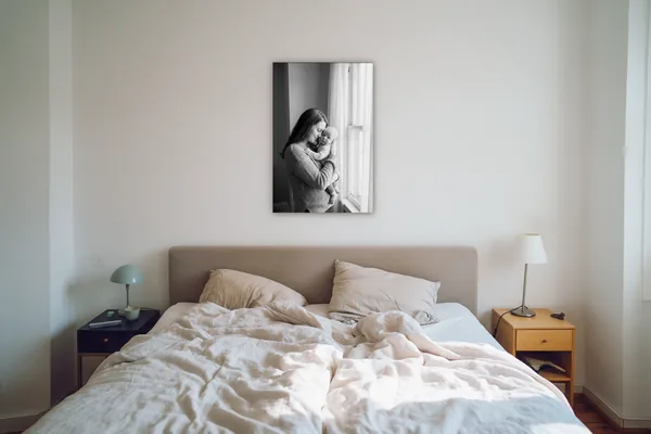 Visualisierung: Schwarzweißfoto einer Mutter mit Baby als Wandbild im Hochformat über einem Bett