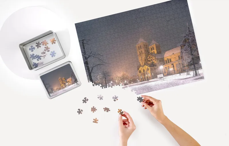 Puzzle mit dem Motiv Dom im Schnee, daneben Schachtel und Puzzleteile