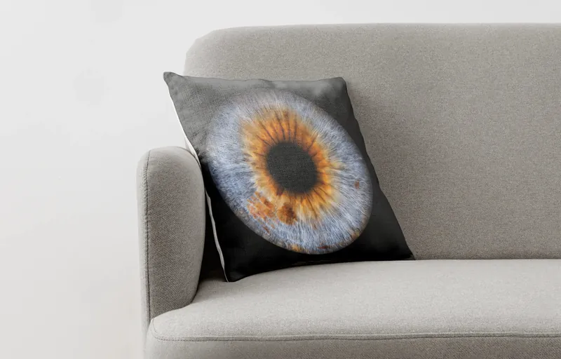 Irisbild auf einem Fotokissen auf einem grauen Sessel – blaue Iris mit orangem Kern auf schwarzem Grund