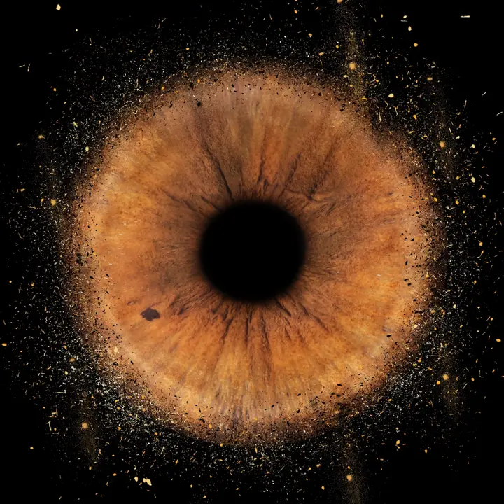 Irisbild mit Explosion-Effekt: braune Iris, deren Rand in goldene Partikel zerstäubt, auf Schwarz – Muster Artikel-Nr. 0122 von JALES – feine Motive in Münster