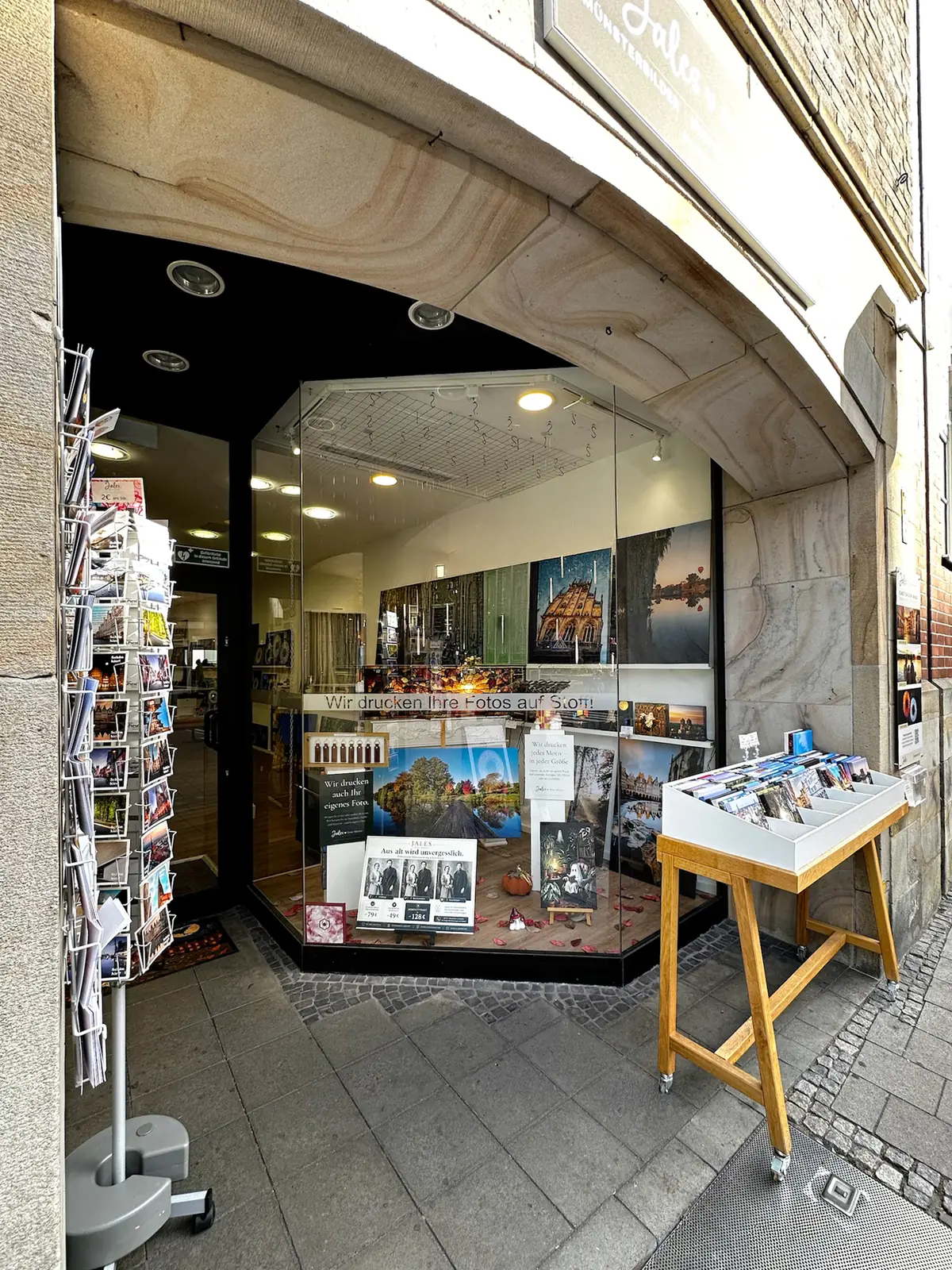 Ladeneingang von JALES – feine Motive unter dem Sandsteinbogen an der Windthorststraße 48 in Münster, mit Blick ins beleuchtete Schaufenster
