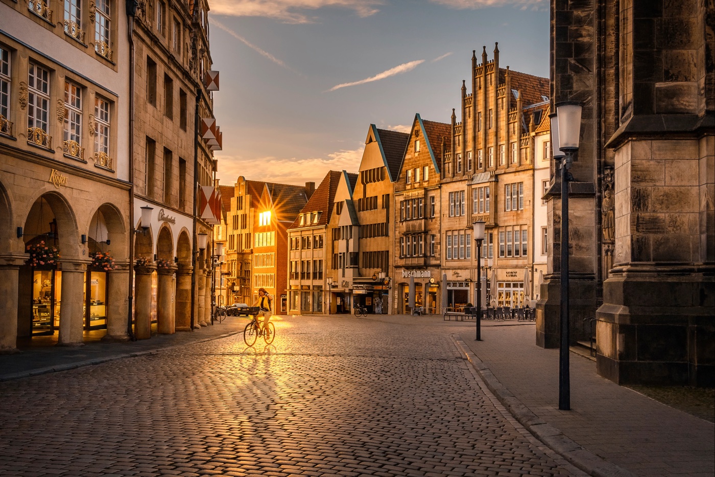 Prinzipalmarkt Münster in der goldenen Stunde – Sonnenstern zwischen den giebelständigen Bürgerhäusern, leeres Kopfsteinpflaster, eine Leeze im Bild. Foto © Sascha Talke.