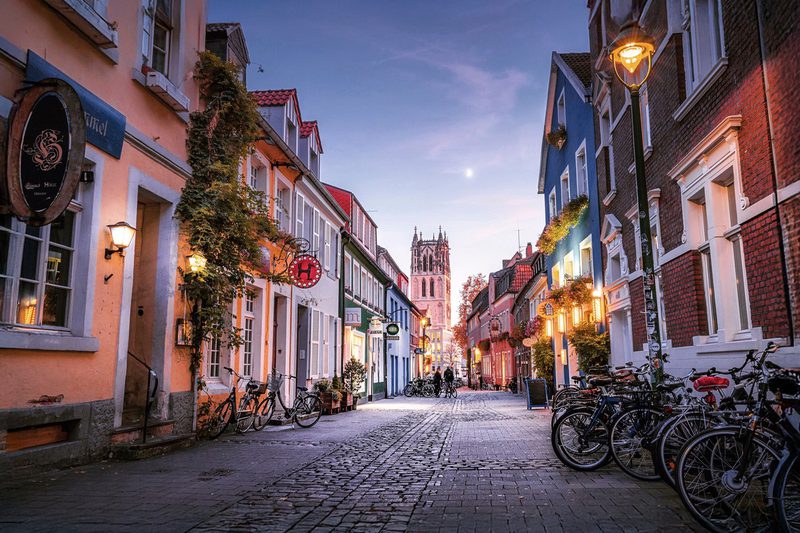 Kuhviertel in Münster am Abend, Gasse mit Fahrrädern und Kirchturm – Münsterbild als Wandbild bei JALES – feine Motive