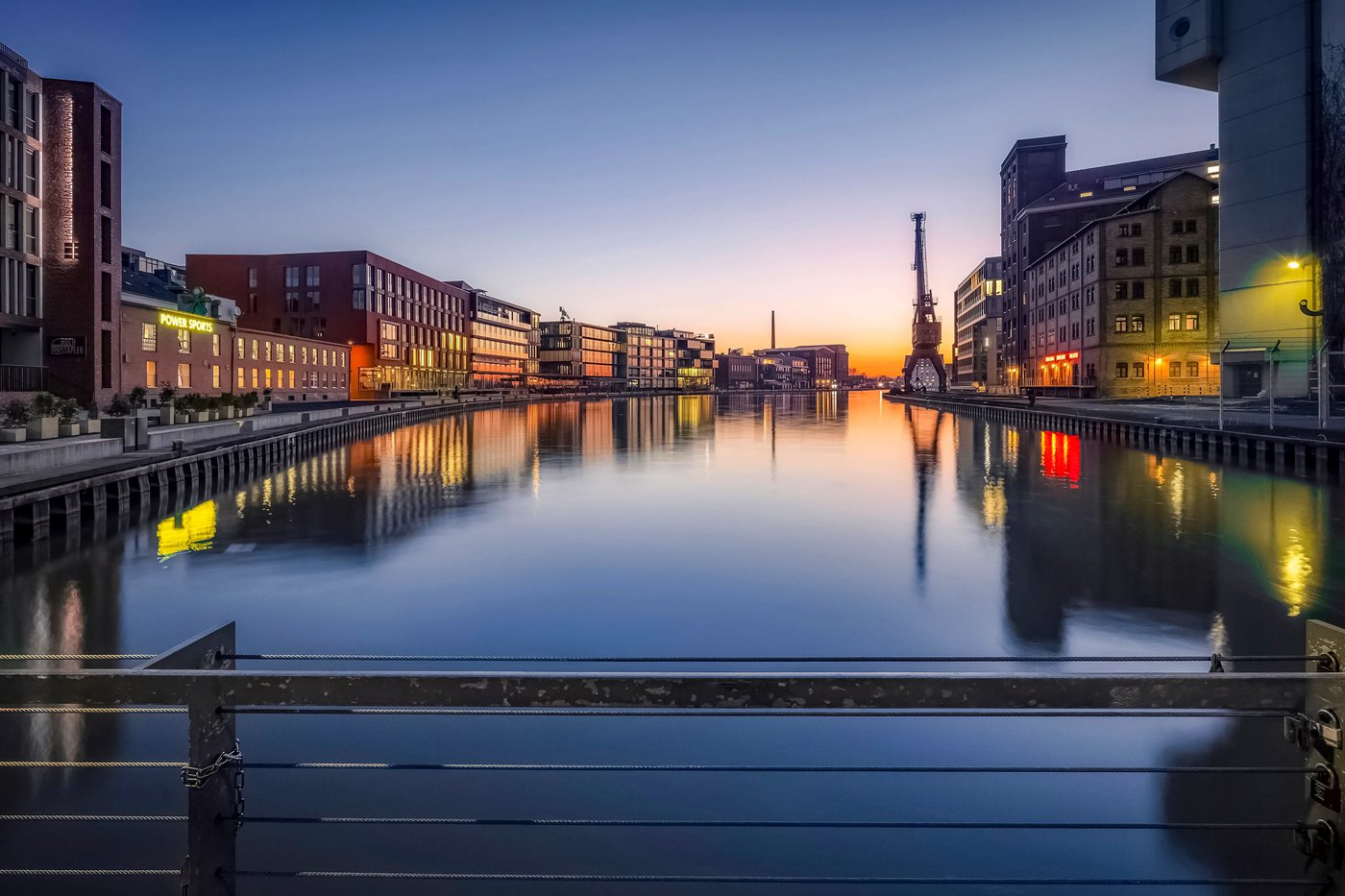 Stadthafen Münster am Kreativkai zur blauen Stunde – spiegelglattes Hafenbecken, der alte Verladekran als Silhouette, letztes Abendrot hinter den Speichern. Foto © Thomas Branse.